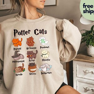 Peut inclure: Un sweat-shirt beige avec un graphique de chats avec des noms de personnages d'Harry Potter. Le texte "Potter Cats" est en haut du graphique. Les noms des chats sont : Rownald, Hermoine, Pawdamort, Meowgonagall, Purrter, Meowfox, Nyaville, Seffurus et Dumpldore.
