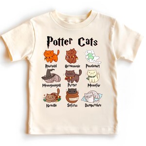 Peut inclure: Un t-shirt cr&egrave;me avec un graphique de chats repr&eacute;sentant des personnages de la s&eacute;rie Harry Potter. Le texte "Potter Cats" est imprim&eacute; en noir au-dessus du graphique. Les noms des personnages sont imprim&eacute;s sous chaque chat.