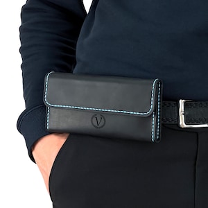 May include: Black leather belt pouch with light blue stitching and a flap closure. The pouch is worn on a black belt with a silver buckle. A circular logo with a "V" is visible on the front.
