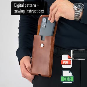 Puede incluir: Una funda de teléfono de cuero marrón con cierre de botón a presión. La funda del teléfono la sostiene una persona. El texto "Digital pattern + sewing instructions" está en la esquina superior izquierda. Iconos PDF y CDR en la esquina inferior derecha.