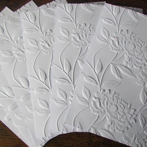 May include: A set of rectangular white cards featuring a raised embossed floral pattern of blooming flowers and leafy vines. The cards are arranged in a fanned-out display, showcasing the textured, three-dimensional surface of the paper.