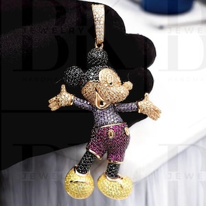 May include: A gold-tone Mickey Mouse pendant charm with black, purple, and red cubic zirconia stones. The pendant is detailed with a black and white Mickey Mouse head and has a gold-tone bail.