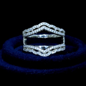 May include: A silver ring setting with a delicate, wavy design encrusted with small, clear gemstones. The ring is displayed on a blue velvet cushion.
