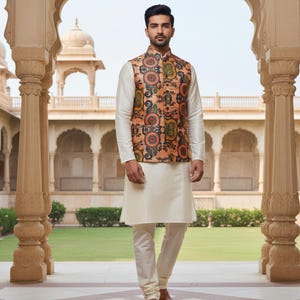 May include: A cream-colored kurta pajama set paired with a patterned vest. The vest features a peach background with circular floral designs in shades of orange, green, and blue. The outfit is worn with brown sandals.