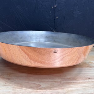 Peut inclure: Une poêle peu profonde de couleur cuivrée avec un intérieur argenté. La poêle a une texture semblable à du bois à l'extérieur et le texte "MADE IN FRANCE" est visible. La poêle est probablement utilisée pour cuisiner ou servir des aliments.