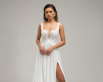 Époustouflante robe de mariée, originale par son décolleté et ses bretelles. La jupe fluide fendue devant offre un magnifique tombé