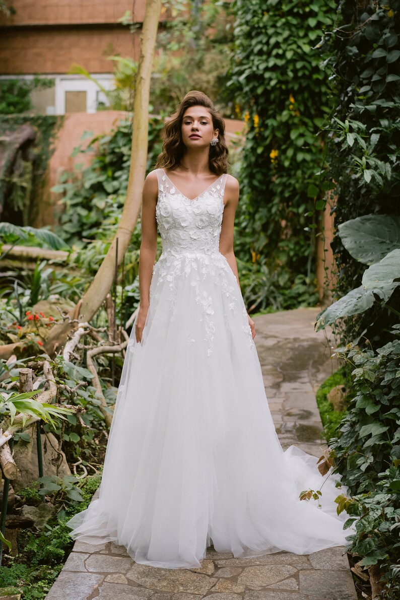 Imaginez vous dans cette robe de mariée envoûtante qui vous transportera dans un univers de féérie le jour de votre mariage. La dentelle florale en 3D ajoute une touche de magie, vous faisant étinceler sous les projecteurs.