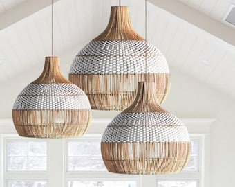 May include: A dining room featuring a large round white table surrounded by six wooden chairs with woven backs and cream cushions. Three large, bell-shaped pendant lights with natural tan and white woven patterns hang above the table.