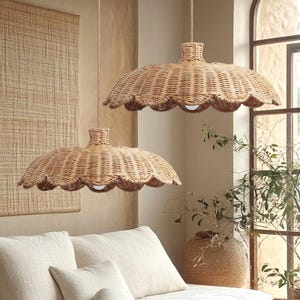 May include: Two woven rattan pendant lights with scalloped edges hang above a low wooden sofa with white cushions. A woven wall hanging and a wooden coffee table complete the neutral-toned, bohemian-style living room.