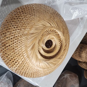 Op de afbeelding: Een ronde, geweven lampenkap gemaakt van natuurlijke bamboe met een spiraalpatroon. De lampenkap is lichtbruin van kleur en heeft een natuurlijke, rustieke uitstraling.