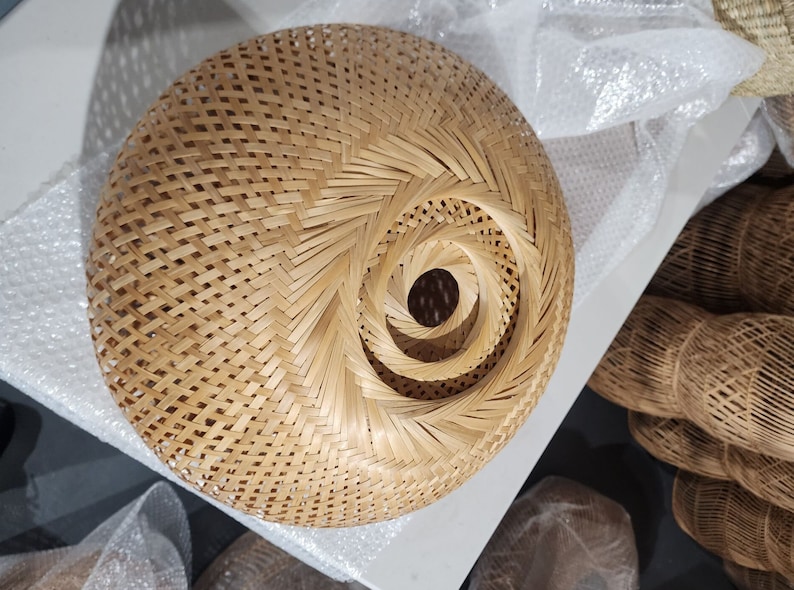 Op de afbeelding: Een ronde, geweven lampenkap gemaakt van natuurlijke bamboe met een spiraalpatroon. De lampenkap is lichtbruin van kleur en heeft een natuurlijke, rustieke uitstraling.