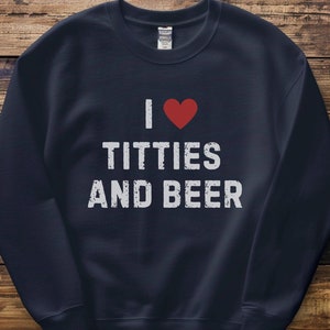 May include: Navy blue sweatshirt with the phrase "I ❤️ TITTIES AND BEER" in white block letters and a red heart. The sweatshirt is a casual garment, likely made of a soft fabric, and suitable for everyday wear.