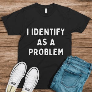Puede incluir: Camiseta negra con texto blanco que dice "Me identifico como un problema".