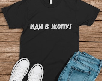 May include: Black t-shirt with the text "ИДИ В ЖОПУ!" printed in white on the front. The shirt is being modeled with a pair of blue jeans and white sneakers.