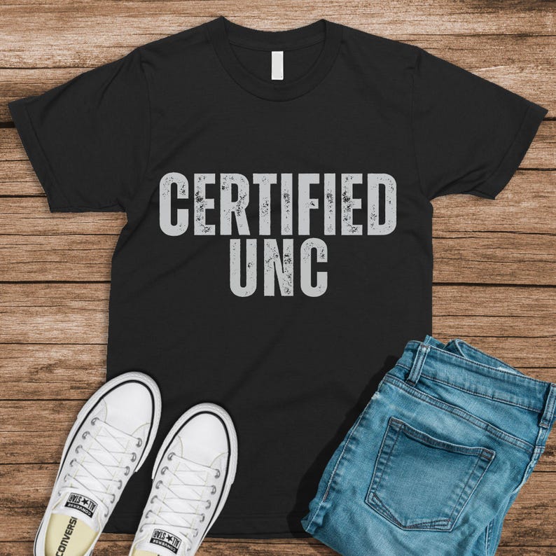 Pu&ograve; includere: Maglietta nera con il testo "CERTIFIED UNC" in bianco, indossata con jeans blu e scarpe da ginnastica bianche.