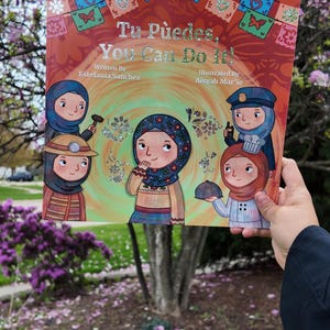 Könnte beinhalten: Ein Kinderbuch mit dem Titel "Tu Puedes, You Can Do It!" zeigt Illustrationen verschiedener Frauen in verschiedenen Berufen. Das Cover-Artwork ist vor dem Hintergrund eines blühenden Baumes platziert. Das Buch wurde von Estefania Sanchez geschrieben und von Aisyah Mar'ie illustriert.