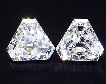 May include: Two clear, triangular-shaped diamonds with a faceted cut. The diamonds are set against a black background.