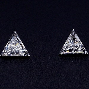 Può includere: Due pietre preziose triangolari trasparenti su uno sfondo nero. Le pietre preziose sono tagliate con molte sfaccettature e hanno una brillante lucentezza.