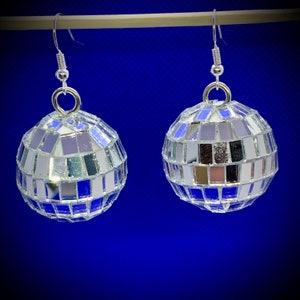 Peut inclure: Une paire de boucles d'oreilles en forme de boule disco argentée. Chaque boucle d'oreille est une petite boule ronde et miroir avec un crochet argenté.