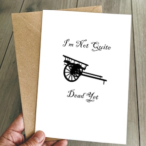 May include: A white card with black text and a black silhouette of a cart. The text reads "I'm Not Quite Dead Yet".
