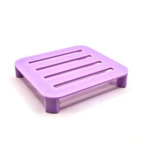 May include: A small, purple plastic soap dish with four raised sides and a grid pattern on the top.