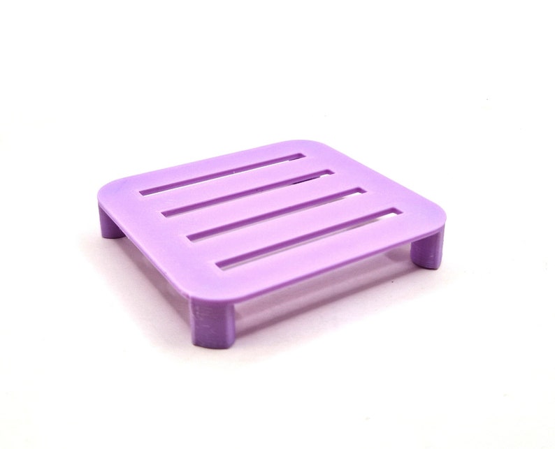 May include: A small, purple plastic soap dish with four raised sides and a grid pattern on the top.
