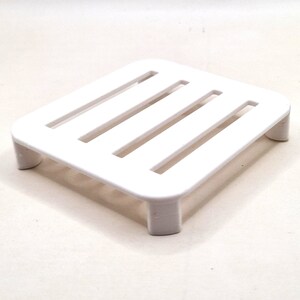 May include: White plastic shelf with five horizontal slats. The shelf has four legs.