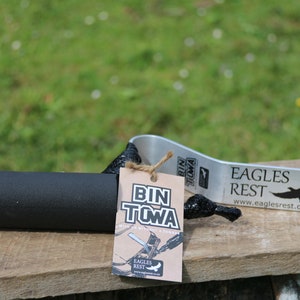 Puede incluir: Una herramienta de remolque de contenedor negra y plateada con un mango de espuma negra y una etiqueta de papel marr&oacute;n que dice "Bin Towa" y "Eagles Rest".