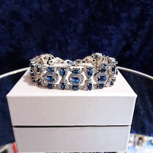 Könnte beinhalten: Ein silbernes Armband mit einer Reihe ovaler blauer Edelsteine, die von kleineren klaren Edelsteinen umgeben sind.