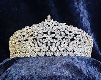 May include: A silver tiara with a large, intricate design of clear, sparkling stones. The tiara is made of metal and has a delicate, feminine look.