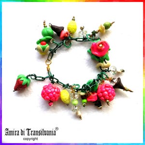 Op de afbeelding: Een groene kettingarmband met bedels van polymer clay. De bedels omvatten aardbeien, frambozen, citroenen, een roos en een klein groen en rood ijsje. De armband is versierd met heldere glazen kralen en gouden accenten. Amira di Transilvania copyright.