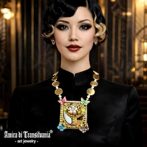 May include: A woman wearing a black top and a statement necklace. The necklace features gold-toned circular links and a large, ornate pendant with colorful embellishments, including butterflies and floral accents. The text "Amira di Transilvania - art jewelry" is visible.