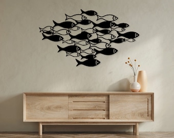 May include: Black metal wall art depicting a school of fish. The artwork is mounted on a light beige wall above a wooden cabinet. The cabinet has a light wood finish and a minimalist design. A vase with dried flowers sits on top of the cabinet.