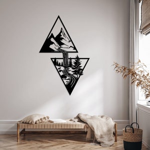 May include: Black metal wall art featuring a geometric design of two triangles. The top triangle depicts a mountain range with a waterfall flowing down into the bottom triangle, which shows a forest scene with a winding path.