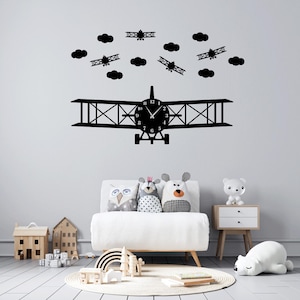 May include: Black and white airplane wall clock with clouds and airplanes around it. The clock is in a nursery with a white couch and pillows.