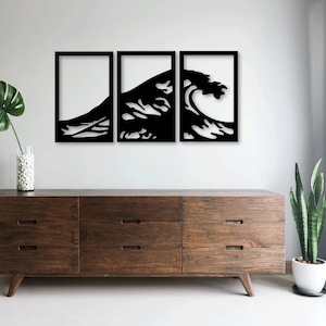 May include: Black metal wall art depicting a large wave crashing. The art is in three separate pieces, each framed in a black rectangle. The art is hanging on a white wall above a dark brown dresser with six drawers.
