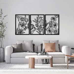 Peut inclure: Trois panneaux muraux en métal noir avec un motif floral. Les panneaux sont disposés horizontalement et présentent différents motifs floraux, notamment des tulipes et d'autres fleurs. Les panneaux sont placés contre un mur blanc dans un salon.