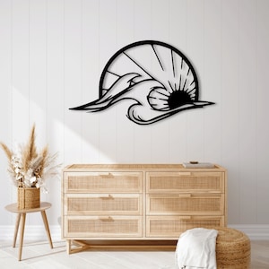 Puede incluir: Arte de pared de metal negro que representa una ola estilizada rompiendo contra un sol. El arte está montado en una pared blanca sobre una cómoda de madera clara con un frente de ratán tejido.