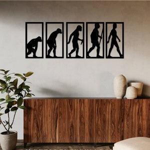 Könnte beinhalten: Ein Satz von fünf schwarzen Metallsilhouetten, die die Stadien der menschlichen Evolution darstellen, montiert an einer hellgrauen Wand über einem dunklen Holzkasten. Die Silhouetten sind in Schwarz gerahmt und in einer Reihe von links nach rechts angeordnet.
