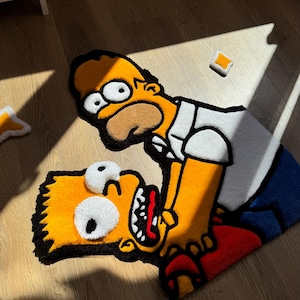 Puede incluir: Una alfombra con Homer y Bart Simpson en una escena juguetona. La alfombra es principalmente amarilla, con detalles en negro, blanco, rojo y azul. Los personajes están representados en un estilo de dibujos animados. También hay pequeñas alfombras cuadradas.