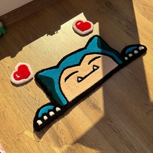 Tufted handmade rug with kawaii sleepy creature design, blue ears and sweet paws peeking from below, surrounded by red hearts. Plush soft pile adds fluffy cozy feel. Perfect as anime rug, cartoon carpet, or kawaii rug décor. Unique handmade rug gift for couples or friends. Adds cheerful cozy charm to bedrooms, nurseries, or creative spaces. Cute rug for playful romantic modern décor