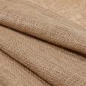 May include: Close-up of a tan fabric with a woven texture. The fabric is folded, showing the interplay of light and shadow across its surface. The material appears to be soft and pliable, with a subtle sheen.