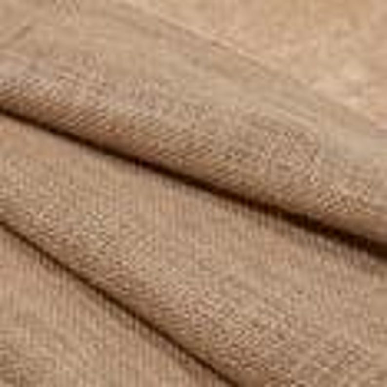 May include: Close-up of a tan fabric with a woven texture. The fabric is folded, showing the interplay of light and shadow across its surface. The material appears to be soft and pliable, with a subtle sheen.