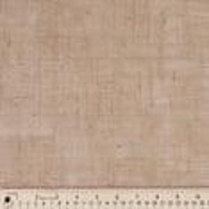 May include: Close-up of a tan linen fabric with a visible woven texture. A ruler with inch markings is placed along the bottom edge, providing a size reference. The fabric appears to be a natural fiber, suitable for various crafting and sewing projects.