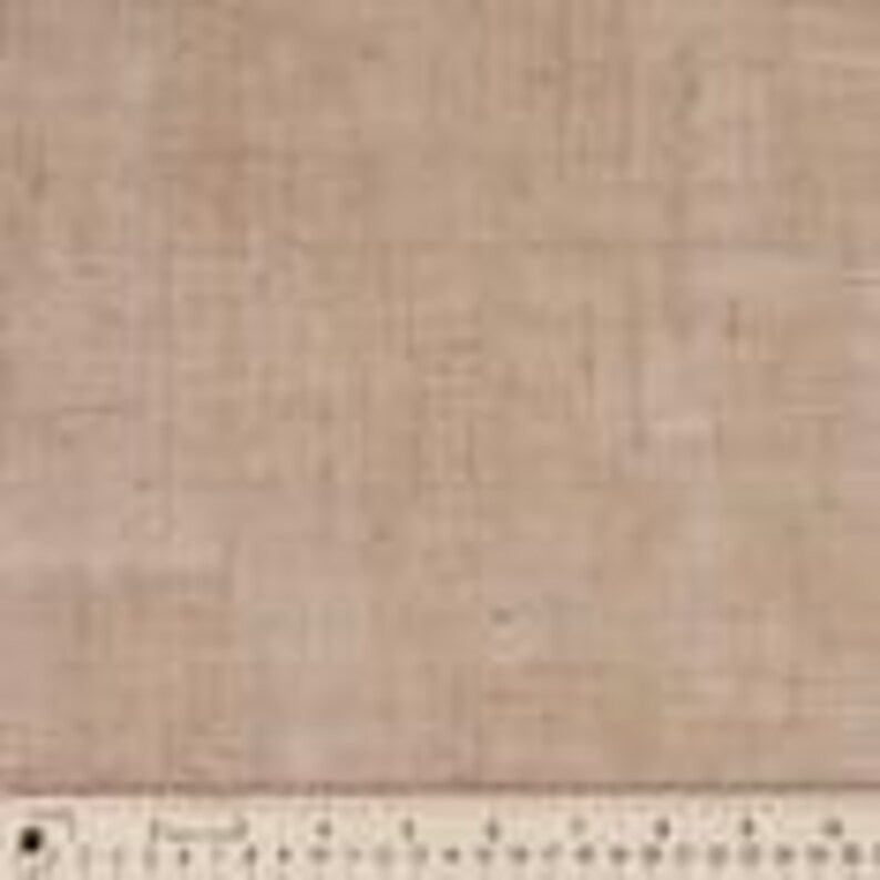 May include: Close-up of a tan linen fabric with a visible woven texture. A ruler with inch markings is placed along the bottom edge, providing a size reference. The fabric appears to be a natural fiber, suitable for various crafting and sewing projects.
