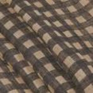May include: Close-up of a fabric with a large checkered pattern. The pattern features alternating squares of dark brown and beige. The fabric appears to be slightly wrinkled, suggesting a soft texture. The weave is visible, indicating a natural fiber.