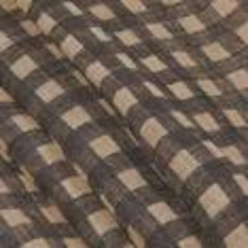 May include: Close-up of a fabric with a large checkered pattern. The pattern features alternating squares of dark brown and beige. The fabric appears to be slightly wrinkled, suggesting a soft texture. The weave is visible, indicating a natural fiber.