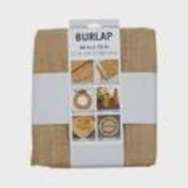 May include: A roll of burlap fabric, wrapped and secured with a white band. The packaging displays the word "BURLAP" and product details. The fabric is a natural tan color, with a visible woven texture. The packaging also shows images of craft projects.