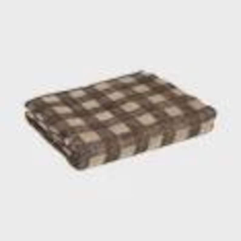 May include: A folded brown and tan plaid blanket. The blanket features a large-scale checkered pattern. The fabric appears soft and cozy, suitable for use as a throw or for layering on a bed. The blanket is rectangular in shape.
