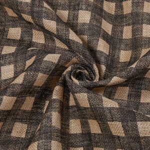 May include: Close-up of a fabric with a repeating checkered pattern. The fabric features a neutral color palette with a dark gray and tan checkered design. The fabric is folded and draped, showing the texture and weave.